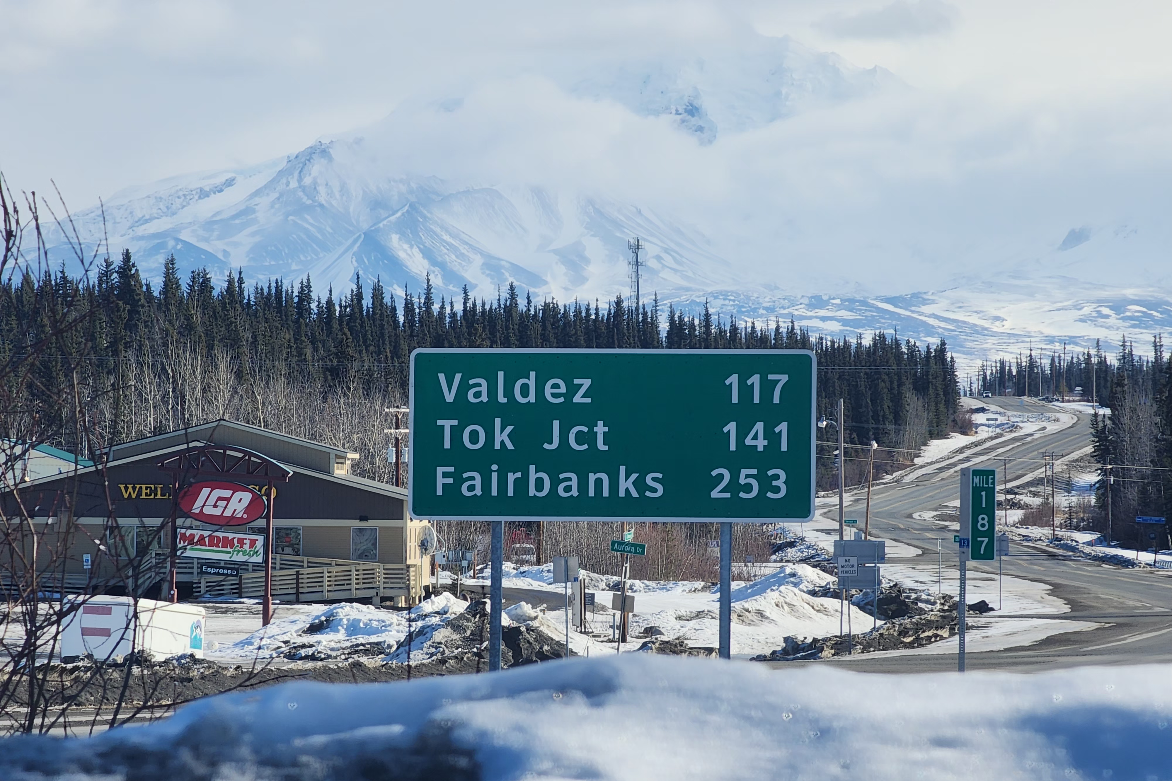 Denali, seen from a roadside in Alaska. Visible in the foreground is a highway sign. Valdez - 117, Tok Jct - 141, Fairbanks - 253