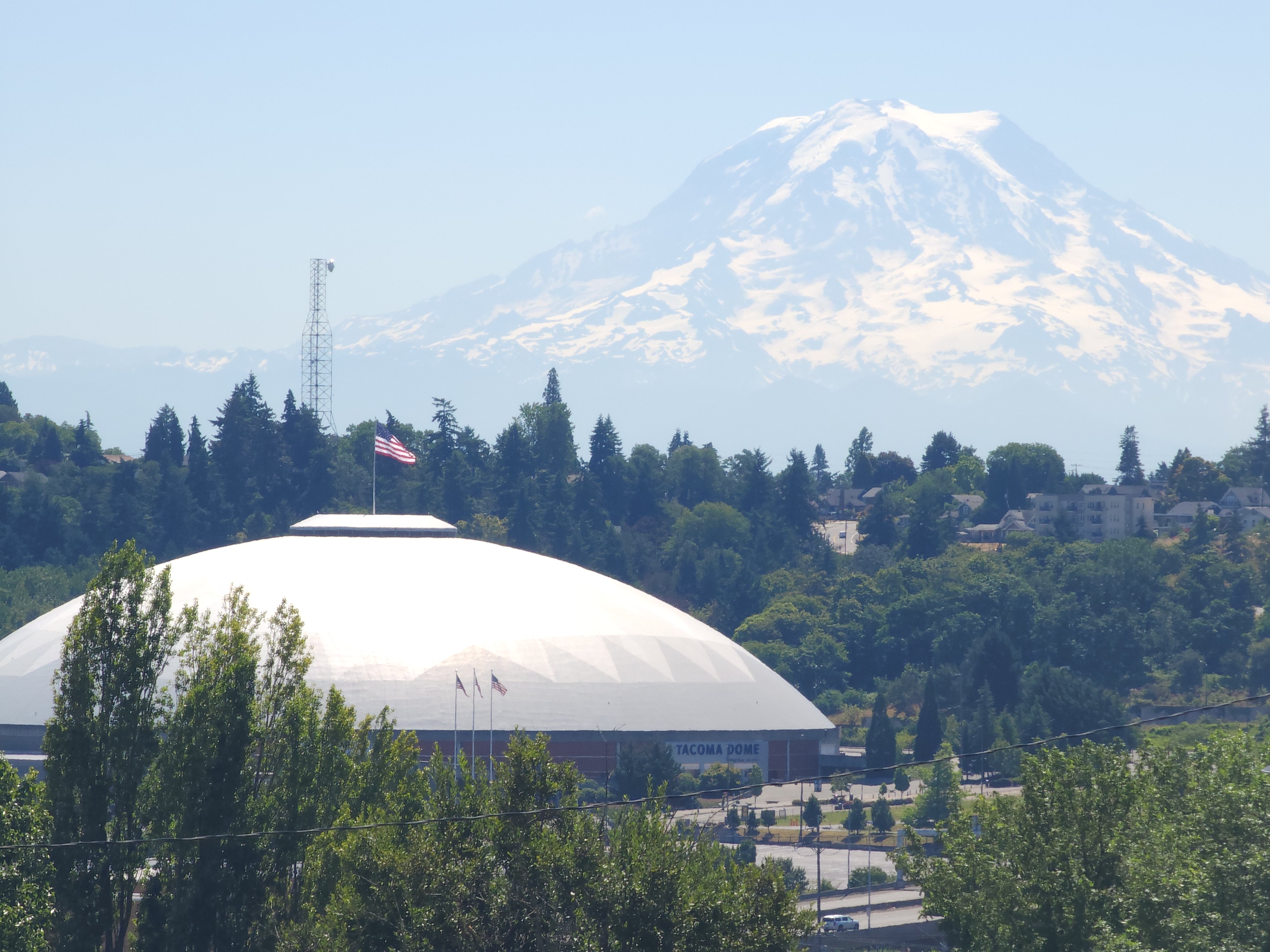 Mount Rainier, viewed from a hillside in Tacoma. In the foreground, the Tacoma Dome is visible as well as some trees.